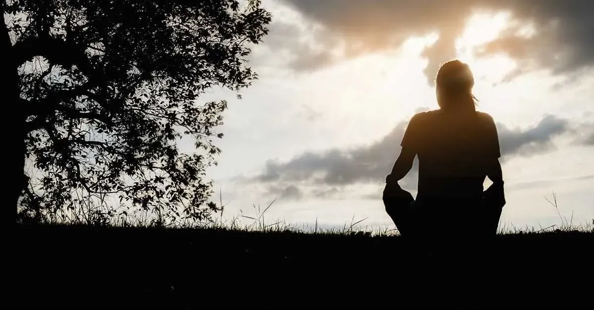 Silhouette di una donna seduta in un prato al tramonto dopo un aborto spontaneo