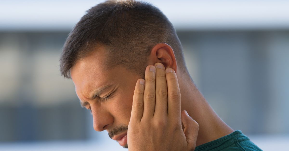 Giovane uomo che si preme l'orecchio per l'acufene