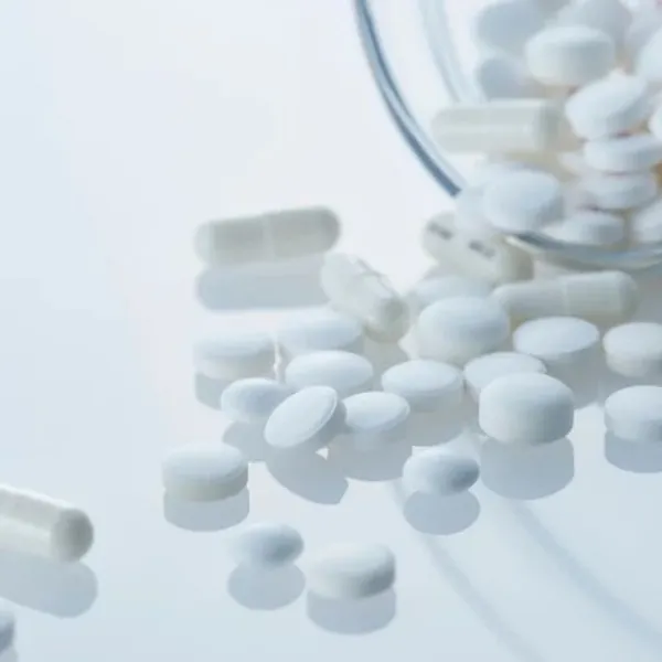 Pillole e capsule bianche uscite da un contenitore di vetro su fondo chiaro