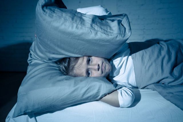 bambino che soffre di insonnia si copre la testa con un cuscino