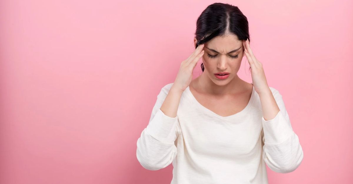 Donna con mani sulle tempie per il mal di testa su sfondo rosa